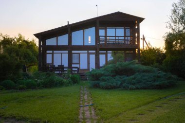 Günbatımında bahçeli modern ahşap ev, huzurlu kırsal yaşam tarzı.