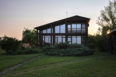 Günbatımında bahçeli modern ahşap ev, huzurlu kırsal yaşam tarzı.