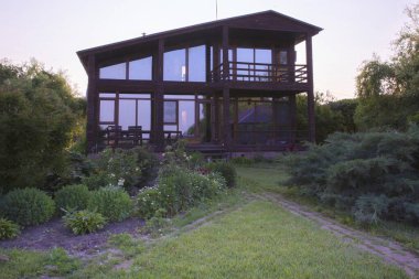 Günbatımında bahçeli modern ahşap ev, huzurlu kırsal yaşam tarzı.