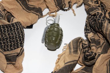 Taktik Shemagh eşarbının ortasına yerleştirilmiş plastik kukla el bombası. Eğitim, simülasyon veya editoryal kullanım için askeri biçim bileşimi.