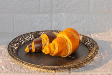 Yuvarlak bir süs tabağında servis edilen taze pişmiş altın ve çikolata kruvasanları. Kahvaltı için mükemmel bir sunum, fırın menüsü, ya da doğal ışık ile yemek fotoğrafçılığı..
