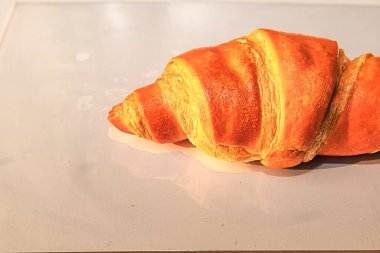 Yumuşak bir arka planda taze pişmiş altın kruvasanın yakın plan görüntüsü. Minimalist yemek imajı fırın ve kahvaltı temaları için mükemmel..