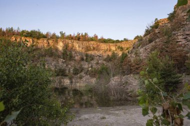 Engebeli taş dokularıyla görkemli kayalık yamaçlar ve sıcak akşam güneşiyle aydınlatılmış dağınık yeşil ağaçlar. Açık gökyüzü ve doğal manzara seyahat, jeoloji ve açık hava temaları için ideal.