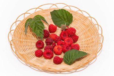 Olgun kırmızı ahududular ve yeşil yapraklar beyaz arkaplanda hasır bir sepete yerleştirilmiş. Organik gıda, yaz hasadı ve sağlıklı yemek kavramı..