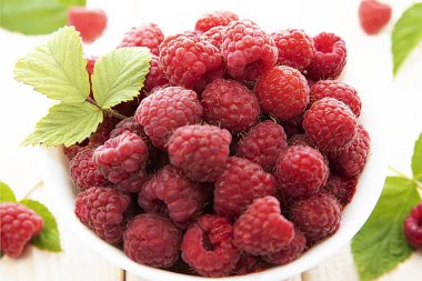 Açık arkaplanlı yeşil yapraklı beyaz bir kasede olgun taze ahududu fotoğrafı. Sağlıklı beslenme, yaz hasadı ve organik gıda kavramı.