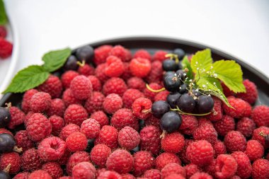 Taze kırmızı ahududular ve yeşil yapraklarla süslenmiş siyah üzümlerle dolu bir kase. Diyet ve sağlıklı yemek için sağlıklı organik yaz meyvesi.