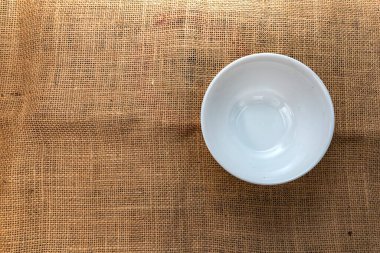 Beyaz seramik kase kırsal bir çuval bezi üzerine yerleştirilmiş, üst manzara. Mutfak modelleri, yemek fotoğrafçılığı, tarif blogları ve doğal mutfak tasarımları için ideal..