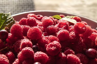 Taze olgun ahududu ve yeşil yapraklar kırsal ahşap masada beyaz bir tabakta. Yaz hasadı, sağlıklı yiyecekler, eko yaşam tarzı, mutfak dekorasyonu ve yemek fotoğrafçılığı konsepti..