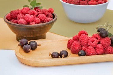 Taze olgun ahududular ve ahşap ve pastel arka planda yaprakları olan seramik kaselerde kuşüzümü. Sağlıklı organik böğürtlen, yaz hasadı, vegan diyeti, asgari ekolojik gıda.