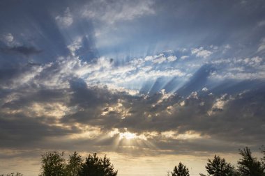 Güneş ışınları çarpıcı mavi gökyüzünde dağınık bulutların arasından kırılıyor. Doğal güneş ışığı ve bulutlu zemin, hava, doğa ve atmosferik ruh hali temaları için mükemmel..