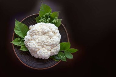 Kıtır beyaz karnabahar yeşil yapraklı, koyu bir tabakta oturuyor, dokusunu ve taze basitliğini vurguluyor..