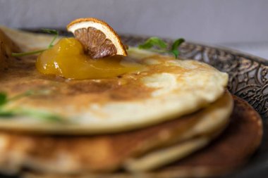 Üzerinde portakal reçeli, kurutulmuş bir dilim ve süslü bir tabakta bitki filizi olan krepler..