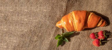 Taze çilek ve fesleğen yapraklarının yanına serpiştirilmiş kahverengi bir kruvasan sıcak, dokulu bir kahvaltı sahnesi oluşturur..