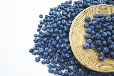 Tahta bir tabakta taze olgun yaban mersini ve beyaz bir arka planda etrafa saçılmış. Vitamin ve antioksidan dolu sağlıklı organik meyveler.