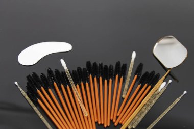 Tek kullanımlık kirpik fırçalar, mikro fırçalar, göz bandı altı ve siyah arka planda metal bir ayna. Kirpik uzantıları, güzellik salonu ve kirpik stilisti için profesyonel araçlar.