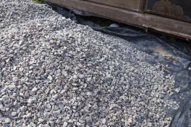 Ahşap bir yapının yanında ezilmiş büyük çakıl taşları yığını. Yol yapımı, beton ve peyzaj projeleri için inşaat malzemeleri.
