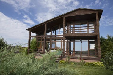 Panoramik pencereli ahşap kulübe ardıç dalları ve mavi gökyüzü ile çevrili, dinlenmek için ideal bir yer, ekolojik turizm ve kırsal tatiller.