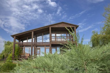 Panoramik pencereli ahşap kulübe ardıç dalları ve mavi gökyüzü ile çevrili, dinlenmek için ideal bir yer, ekolojik turizm ve kırsal tatiller.