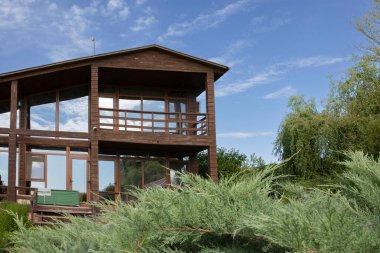 Panoramik pencereli ahşap kulübe ardıç dalları ve mavi gökyüzü ile çevrili, dinlenmek için ideal bir yer, ekolojik turizm ve kırsal tatiller.