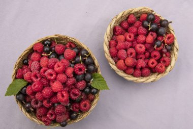 Taze ahududu ve siyah frenk üzümlü sepetler beyaz ve eflatun arkaplanlı, ipli. Yaz meyveleri, sağlıklı organik gıda ve vitaminler..