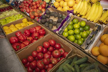 Karton kutularda domates, dolmalık biber, limon, avokado, muz ve portakal gibi renkli sebzeler ve meyvelerin en üst görüntüsü. Sağlıklı gıda ve yerel tarım kavramı.