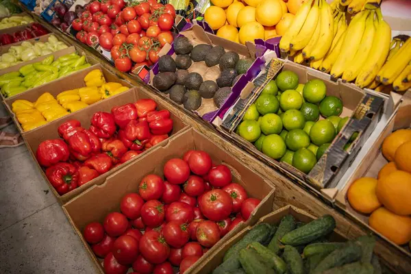 Karton kutularda domates, dolmalık biber, limon, avokado, muz ve portakal gibi renkli sebzeler ve meyvelerin en üst görüntüsü. Sağlıklı gıda ve yerel tarım kavramı.