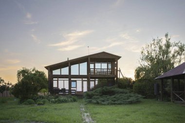 Günbatımında yeşil bir bahçede panoramik pencereli modern ahşap ev mimari ve emlak kavramları için idealdir.