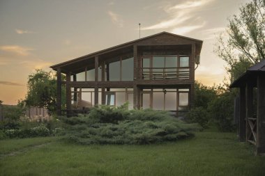 Günbatımında yeşil bir bahçede panoramik pencereli modern ahşap ev mimari ve emlak kavramları için idealdir.