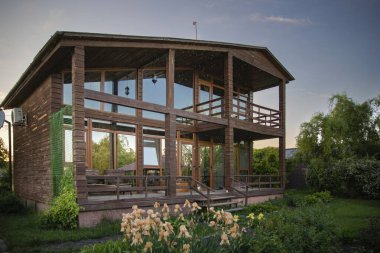 Gün batımında bahçesinde büyük pencereleri olan rahat ahşap bir ev. Tatil yaşam tarzı ve kırsal rahatlama kavramları için mükemmel.