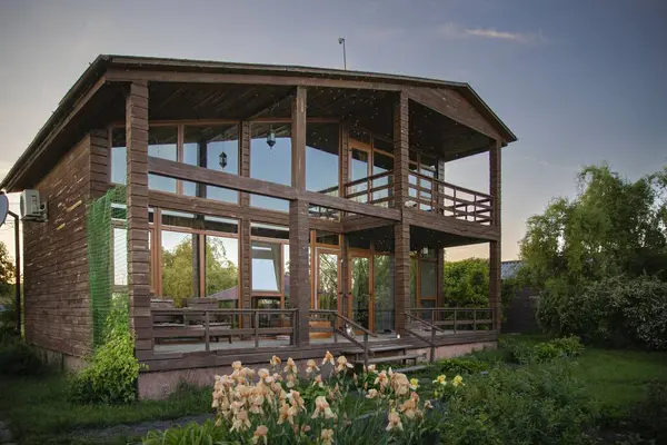 Gün batımında bahçesinde büyük pencereleri olan rahat ahşap bir ev. Tatil yaşam tarzı ve kırsal rahatlama kavramları için mükemmel.