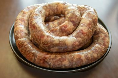 Siyah bir tabağa sarılmış taze çiğ sosis yakın plan. Geleneksel et ürünü ızgara, sigara ve yemek için hazır..