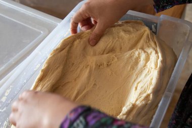 Plastik bir kabın içinde taze hamuru geren elleri kapatın. Çiğ hamur hamuru ile ev yapımı pişirme işlemi. Ekmek ya da pizza için..