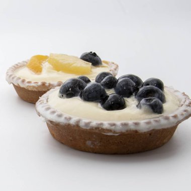 Kremalı kremalı iki meyveli turtayı kapat. Birinde yabanmersini, diğerinde kivi, şeftali, ananas ve yabanmersini var. Gurme ve fırın temaları için lezzetli bir tatlı..