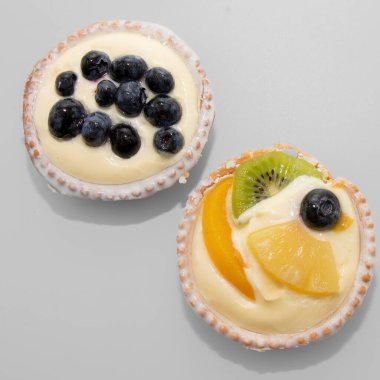 Kremalı kremalı iki meyveli turtayı kapat. Birinde yabanmersini, diğerinde kivi, şeftali, ananas ve yabanmersini var. Gurme ve fırın temaları için lezzetli bir tatlı..