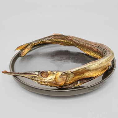 Tütsülenmiş çelenk siyah bir tabakta daire şeklinde dizilmiş. Geleneksel deniz ürünleri lezzeti, altın sarısı tenli, servis yapmaya hazır..