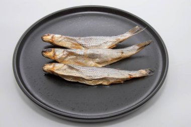 Siyah bir tabağa dizilmiş üç kurutulmuş balık. Geleneksel deniz ürünleri atıştırmalıklar, bira eşliğinde ya da yemek pişirmek için..