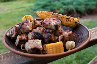 Bahçedeki bir tabakta servis edilen kızarmış mısırla ızgara domuz eti parçalarını kapatın. Barbekü pikniği ve yaz yemeği kavramları için mükemmel.
