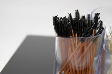 Çevre dostu bambu saplı profesyonel rimel spoolie fırçaları şeffaf bir kapta saklanıyor, beyaz ve siyah arka planda yakın plan. Güzellik, makyaj ve kirpik uzatma temaları için mükemmel.