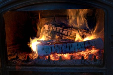 Parlayan alevler ve sıcak közlerle yanan odunları kapatın. Ev konforu ve rahatlığı için sıcak şöminenin arka planı.