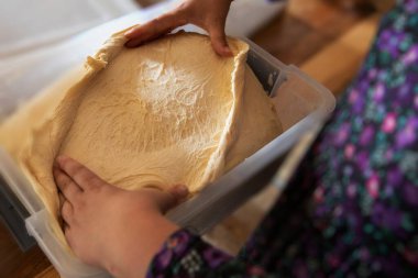 Plastik kabın içine hamur mayası koyan kadınların ellerini kapatın. Geleneksel aile yemekleri ve ev yapımı hamur işleri.