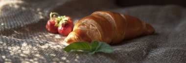 Doğal ışık altında, kırsal kumaş arka planında taze çilekli kruvasan.