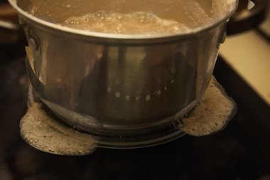 Yulaf lapası kaynıyor ve metal bir tencerenin kenarından fırına dökülüyor. Yemek pişirme, ev yapımı yemek, mutfak kazası ve günlük yaşam tarzı kavramı..