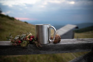 Karabina saplı metal kupa ve kırsal ahşap çitlerin üzerindeki böğürtlen manzaralı dağ manzarası ve ahşap kulübe. Kamp, yürüyüş, doğa gezisi ve eğlenme kavramı..