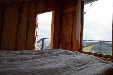 Yatak ve beyaz yataklı ahşap kırsal yatak odası. Pencereden dağlara bak. Çevresel yaşam tarzı kırsal turizm ve doğada rahatlama kavramı.