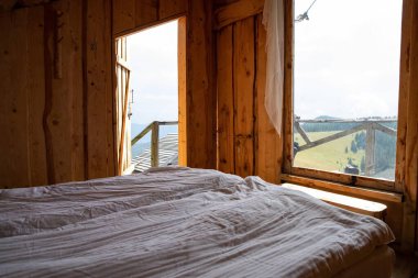 Yatak ve beyaz yataklı ahşap kırsal yatak odası. Pencereden dağlara bak. Çevresel yaşam tarzı kırsal turizm ve doğada rahatlama kavramı.