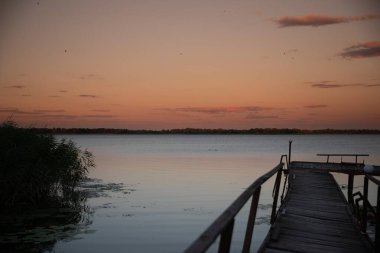 Gün batımında göle giden tahta iskelenin manzarası sakin bir su ve renkli bir gökyüzü rahatlama seyahati ve huzurlu doğa konseptiyle.