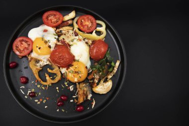 Izgara sebzeli sahanda yumurta ve siyah tabakta domates. Sağlıklı kahvaltı kavramı.