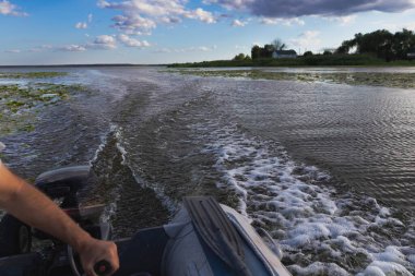 Kırsal alanda ve mavi gökyüzünde köpüklü su yolu olan nehirde sürat teknesi gezintisi. Seyahat, balıkçılık, eğlence ve doğa kavramı