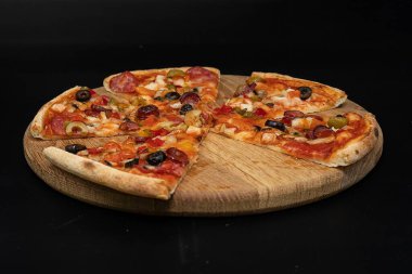 Siyah arka planda tahtadan servis edilen sosisli, sebzeli, peynirli ve zeytinli pizza. İtalyan yemeği, fast food, akşam yemeği, restoran menüsü ve teslimat kavramı.