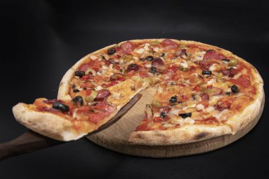 Tahta tahtada servis edilen sosisli, sebzeli, peynirli ve zeytinli pizza, spatulada bir dilim kaldırıldı. İtalyan mutfağı, restoran menüsü, fast food, teslimat ve ev yapımı yemek kavramı..